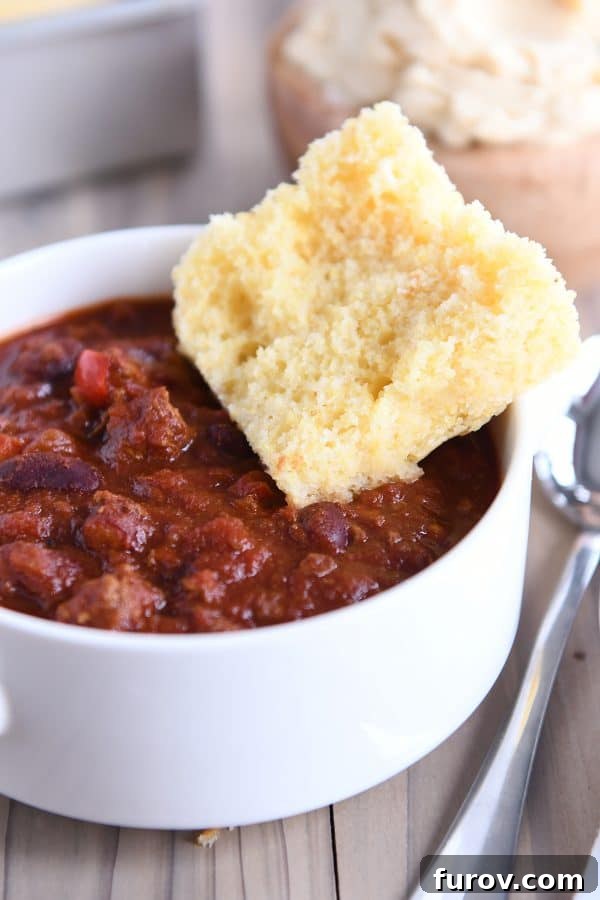 A hearty piece of fluffy cornbread resting beside a warm bowl of chili, ready to be dipped.