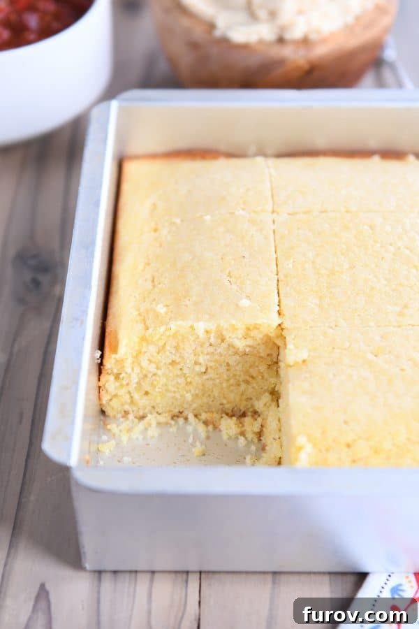 A freshly baked pan of golden cornbread with a single perfect slice removed, showcasing its tender texture.