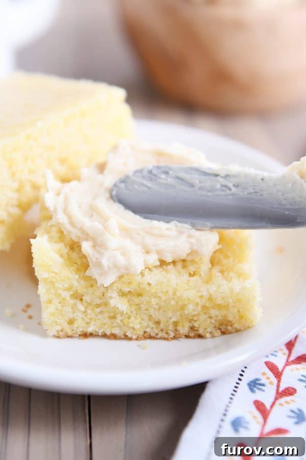 A hand gently spreading luxurious fluffy honey butter onto a warm, golden slice of cornbread.