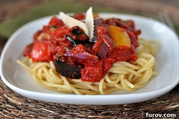 White plate with cooked spaghetti noodles topped with a chunky red sauce.