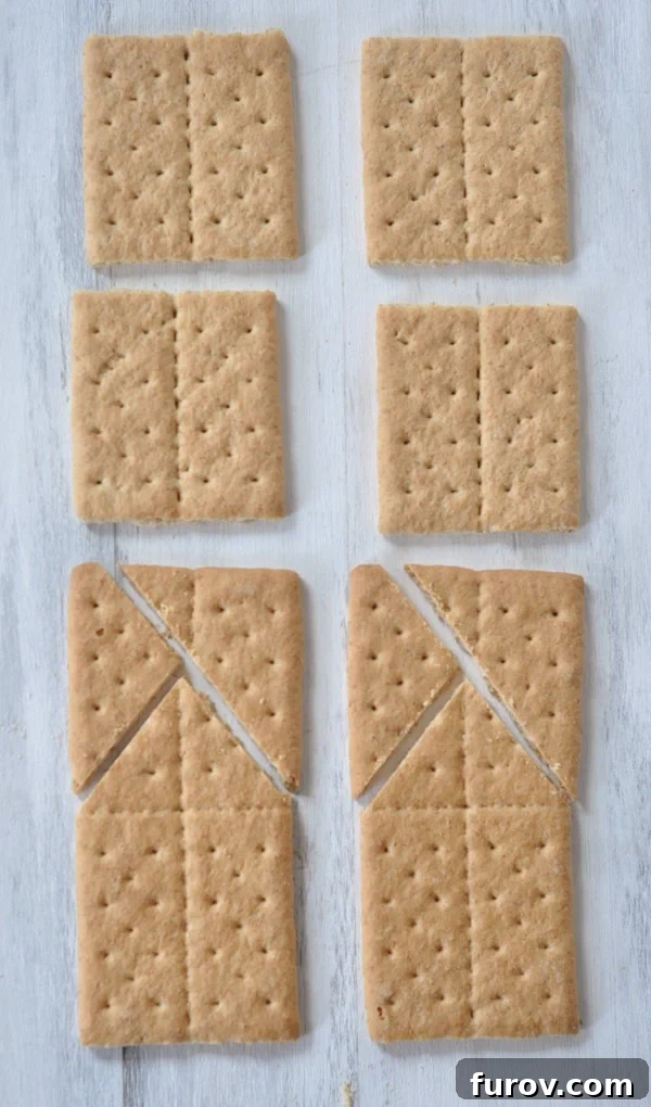Top-down view of graham crackers laid out on a cutting board, demonstrating how to break and score them for house components