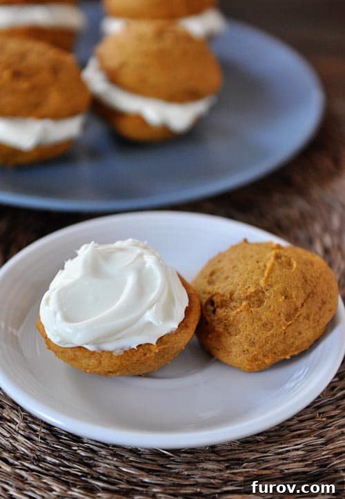 Pumpkin Spice Cream Sandwich Cookies 2 A pumpkin cream sandwich on a white plate with the top of the cookie sitting on the side.