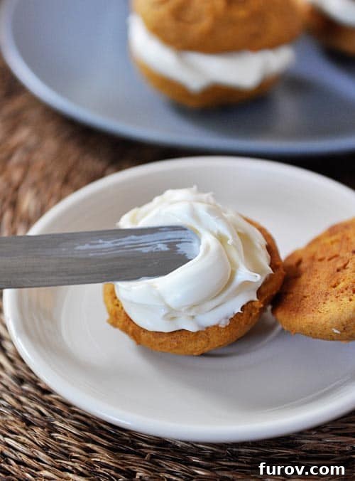 Pumpkin Spice Cream Sandwich Cookies 4 A pumpkin cookie getting frosted with a metal offset spatula.