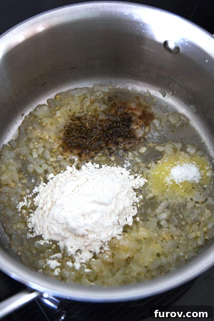 Top down view of a metal pot with sautéed onions, aromatic spices, and flour forming a roux.