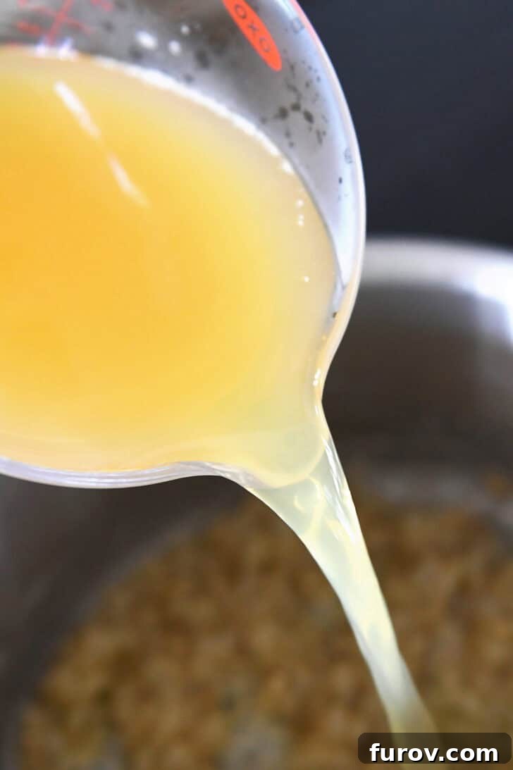 A measuring cup carefully pouring rich chicken broth into a stock pot, creating the base for the sauce.