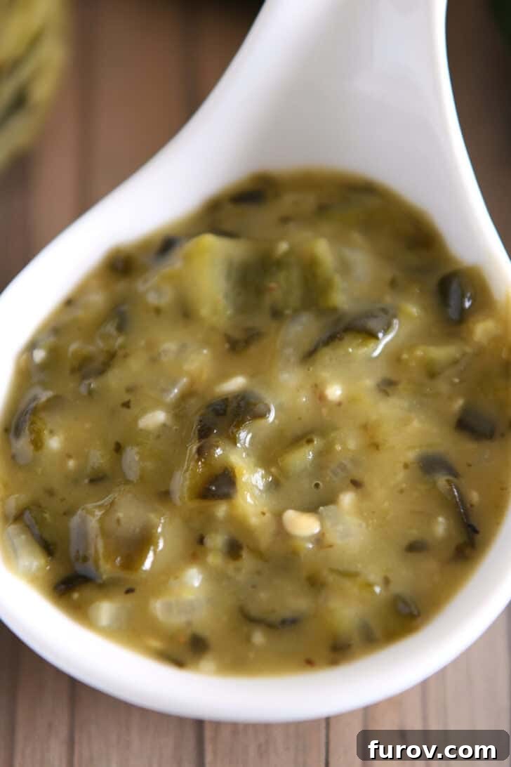 Top down view of a white ladle filled with rich, homemade green enchilada sauce, glistening under the light.