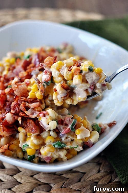 A serving of creamy confetti corn and bacon, with a spoon scooping a generous portion, highlighting its rich texture and colorful ingredients.