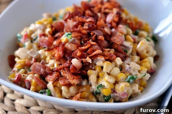 A beautifully presented bowl of creamy confetti corn, generously topped with golden-brown, crispy chopped bacon bits, ready to be served.