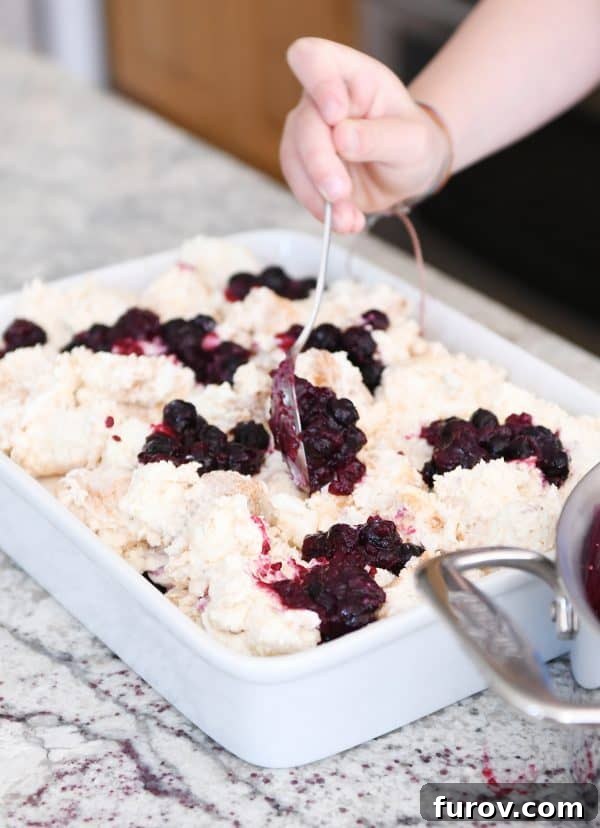 A hand carefully spooning the vibrant, thick blueberry filling over the creamy angel food cake base in a serving dish.
