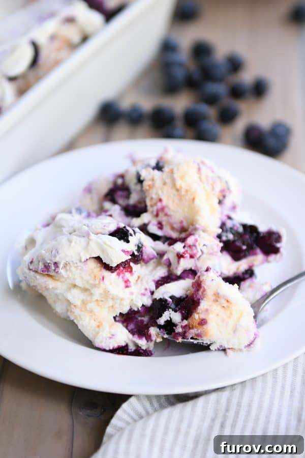 A pristine white dessert plate holding a generous scoop of heavenly blueberries and cream angel food cake dessert, with a spoon taking a perfect bite.