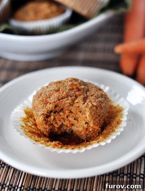 Healthy Carrot Cake Muffins with Applesauce 10 A healthy carrot cake muffin with one bite taken out, sitting on a peeled-off white liner.