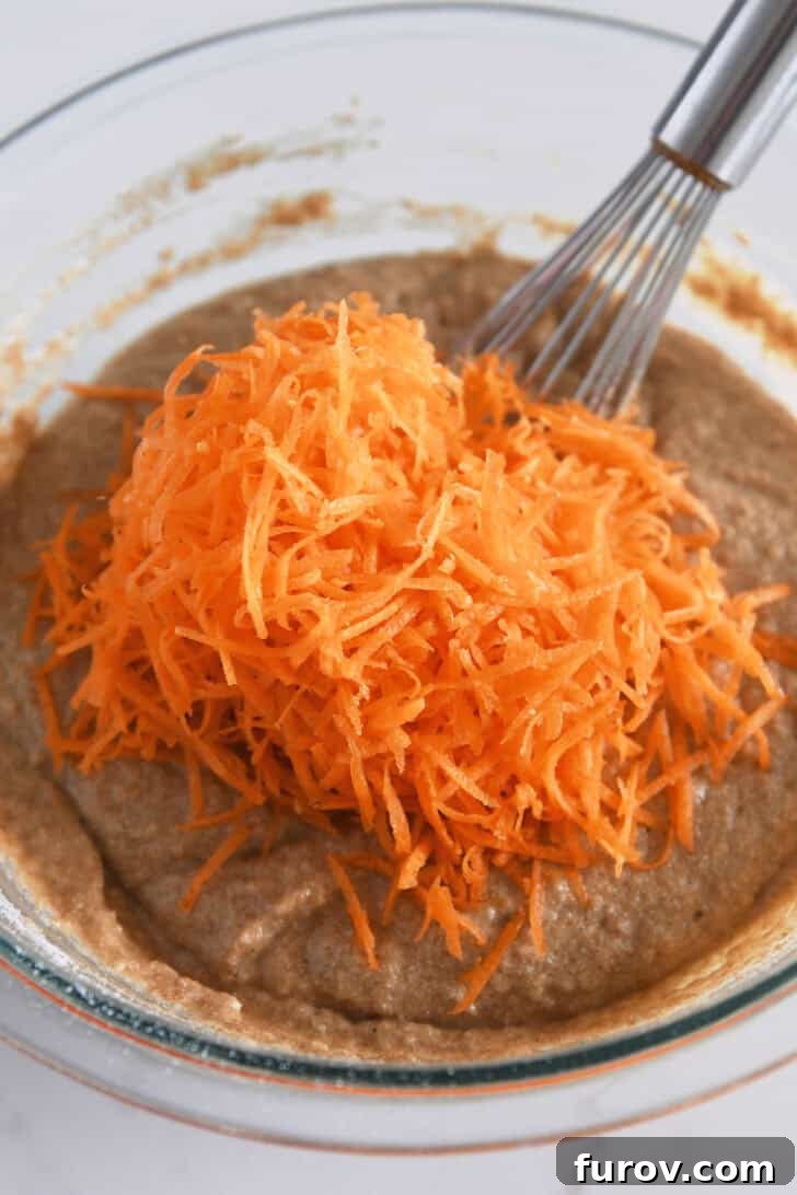 Healthy Carrot Cake Muffins with Applesauce 4 Finely shredded carrots being folded into the carrot cake muffin batter in a glass bowl.