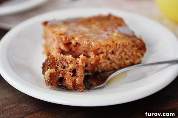 A piece of apple cake with sauce on top with a fork taking a bite out.