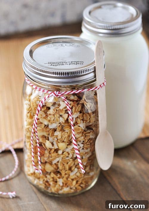 A elegant mason jar overflowing with homemade coconut granola, tied with a ribbon and spoon, standing beside a jar of creamy yogurt.