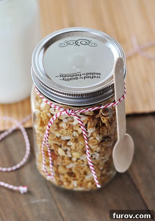 A beautifully presented mason jar filled with homemade coconut granola, adorned with a spoon and elegant ribbon.