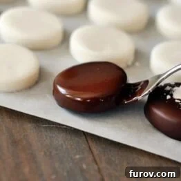 A hand dipping homemade peppermint patty in melted chocolate, showcasing the ease of the process.