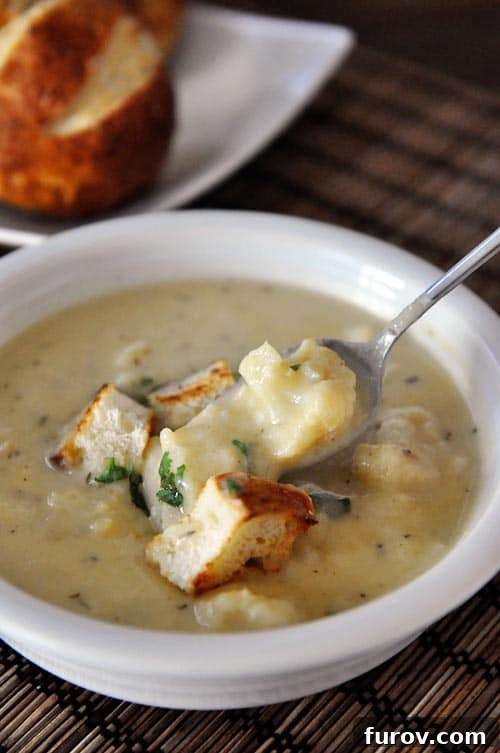 White bowl of roasted cauliflower soup with croutons on top and a spoon taking a bite out.