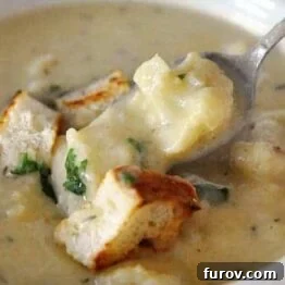 A bowl of creamy roasted cauliflower and white cheddar soup, garnished with fresh parsley and croutons.
