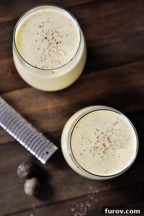 Top view of two glass cups full of eggnog sprinkled with freshly grated nutmeg.
