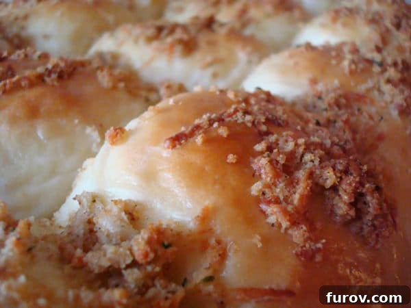 Close up of a baking pan filled with golden brown parmesan and herb crusted rolls, fresh from the oven.
