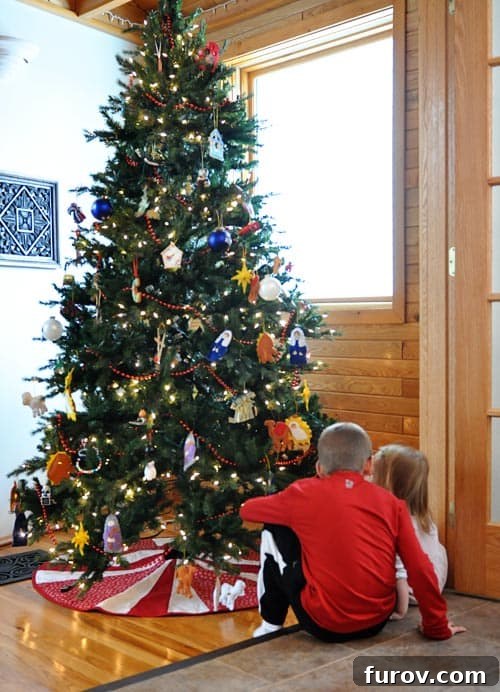 Our Beloved Holiday Rituals Captured This Weekend 2 Little kids sitting by a beautifully decorated Christmas tree, surrounded by festive ornaments and warm lights.