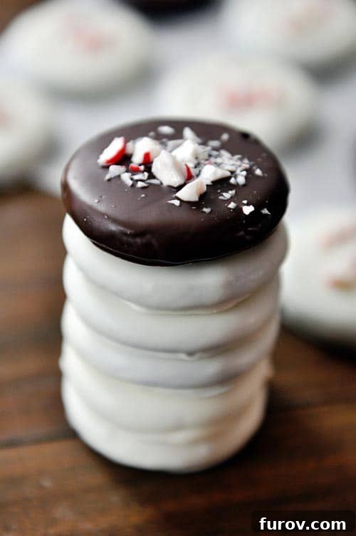 A perfectly stacked tower of homemade thin mint cookies, some dipped in white chocolate and adorned with crushed candy canes, showcasing their irresistible minty goodness.