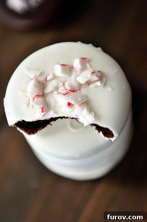 A close-up of a white chocolate-dipped homemade thin mint cookie with a bite taken out, revealing the dark chocolate cookie beneath and festive crushed candy canes on top.