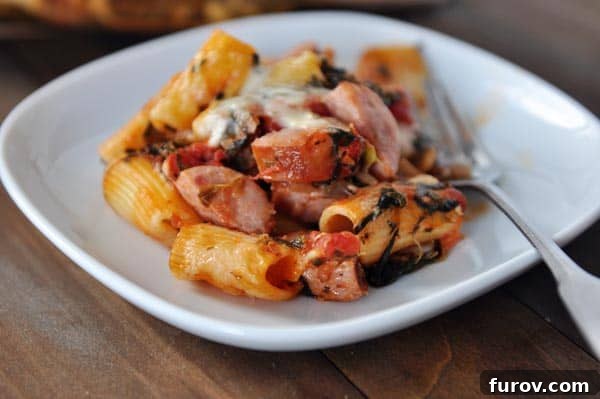 Savory Chicken Sausage Pasta Bake 3 White plate with cooked tube pasta, slices of chicken sausage, and melted cheese.