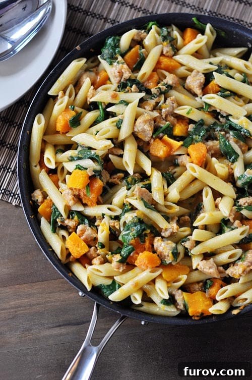 A skillet full of tube pasta, butternut squash, spinach, and sausage, perfectly cooked and ready to serve.