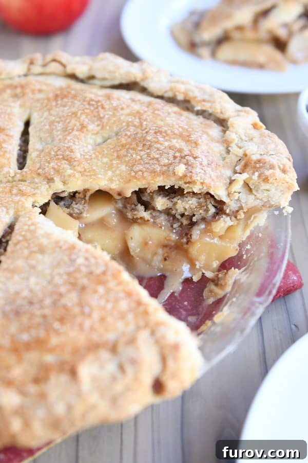 Golden Toffee Crunch Caramel Apple Pie 3 A freshly baked Toffee Crumble Caramel Apple Pie in a glass pie plate with one slice removed, revealing the golden crust and bubbling filling.