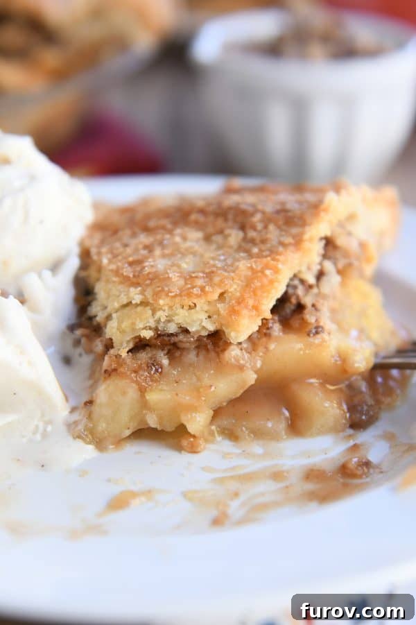 Golden Toffee Crunch Caramel Apple Pie 7 Half a slice of Toffee Crumble Caramel Apple Pie on a white plate, served with a generous scoop of vanilla ice cream.