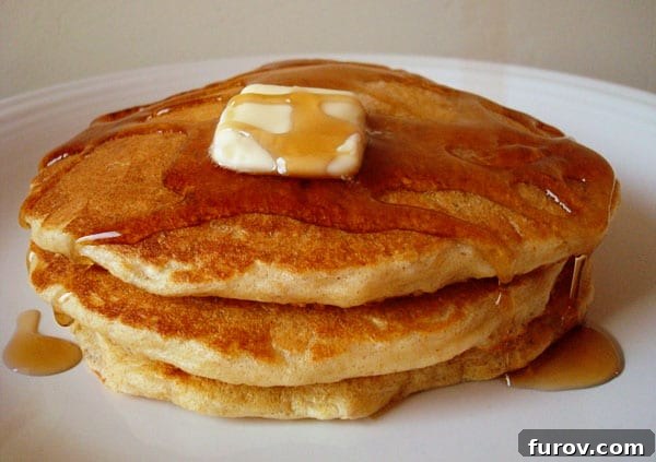 A stack of golden oatmeal pancakes, drizzled with syrup and topped with a pat of melting butter.