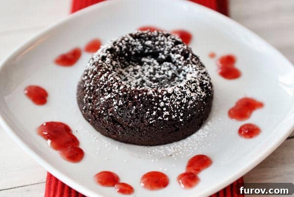 A beautifully presented chocolate molten cake, dusted with powdered sugar, sitting on a white plate with a vibrant raspberry sauce drizzled alongside.