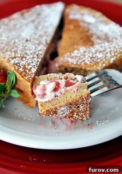 A perfectly cooked strawberry cream stuffed French toast, dusted with powdered sugar, with a bite taken out revealing the luscious filling. Garnished with fresh mint.