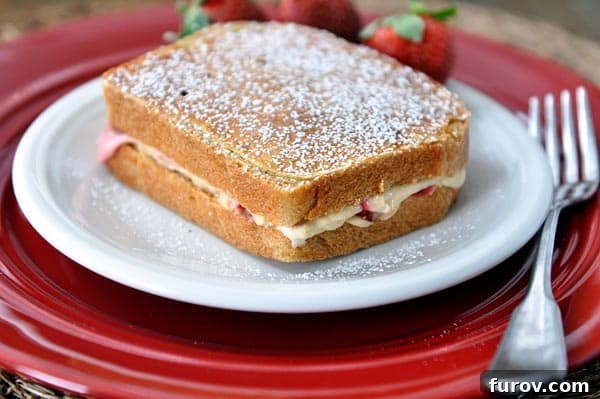 A single piece of strawberries and cream stuffed French toast dusted with powdered sugar, served elegantly on a white plate, ready to be enjoyed.