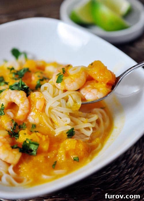 A beautiful white bowl filled with delicate rice noodles, generously coated in a rich, vibrant butternut squash and coconut curry sauce, topped with succulent, perfectly cooked shrimp, garnished with fresh herbs.
