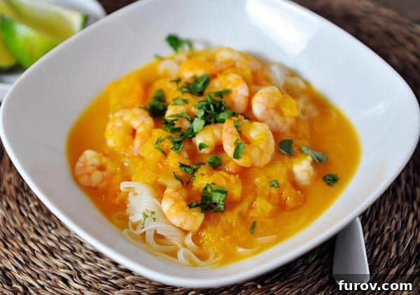 A close-up of a serving of shrimp curry sauce over rice noodles in a crisp white bowl, ready to be enjoyed.