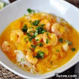 Butternut squash and coconut curry soup with shrimp and rice noodles, garnished with fresh cilantro and lime.