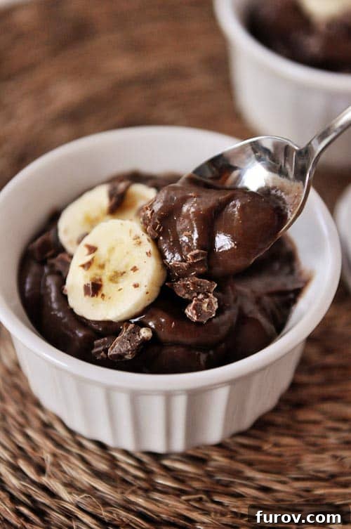 Incredible Chocolate Pudding Free From Dairy Eggs and Gluten 2 A white ramekin with dark chocolate pudding topped with banana slices and chocolate. A spoon is taking a bite out.