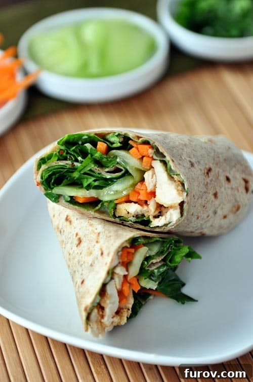 A chicken and vegetable-filled wrap split in half on a white plate, showcasing its vibrant contents.