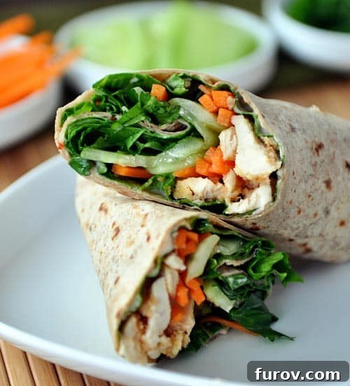 A vibrant chicken and vegetable wrap neatly split in half on a clean white plate, highlighting the fresh, crisp ingredients.