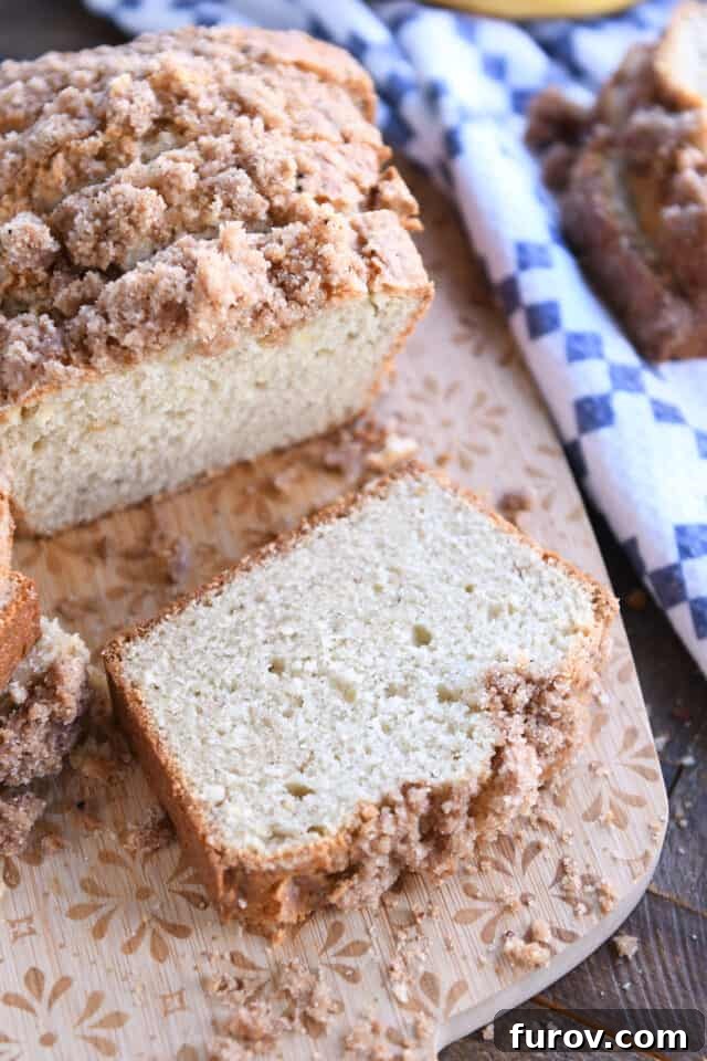 Slice of cream cheese banana bread on cutting board, showcasing its moist texture and cinnamon topping.