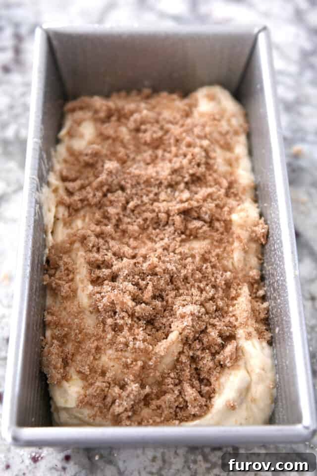 Banana bread batter in a bread pan with sweet cinnamon topping sprinkled generously over the top, ready for baking.