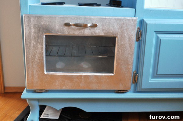 Detailed view of the play kitchen oven with metallic door and plexiglass front
