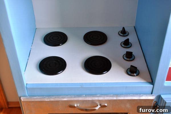 Close-up of the play kitchen stovetop with painted coaster burners and turning knobs