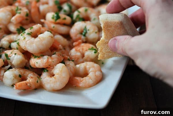 Family Favorite 20-Minute Shrimp Scampi 3 A platter of shrimp scampi with someone holding a half-eaten crusty bread roll over the top, ready for dipping.