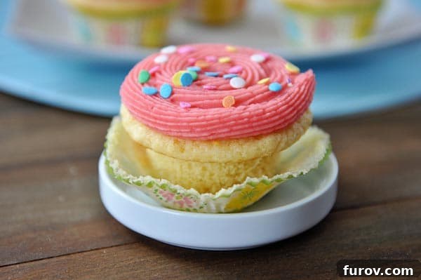 A single yellow cupcake, beautifully frosted with pink icing and colorful sprinkles, nestled in a white ceramic ramekin.