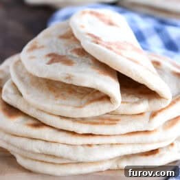 A stack of golden brown flatbread on a wooden cutting board, with a blue and white checkered towel beside it.