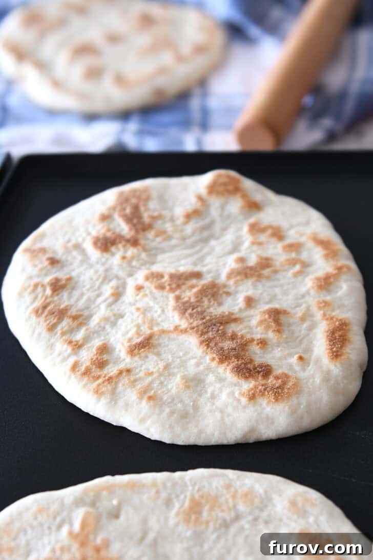Two golden-brown, round flatbreads actively cooking and puffing on a hot griddle, demonstrating the ideal cooking stage.