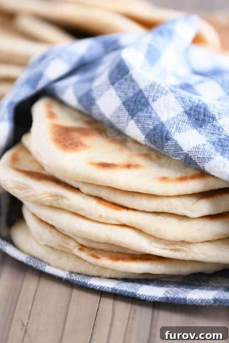 A stack of golden brown flatbreads, lovingly wrapped in a blue and white checkered kitchen towel, keeping them warm and soft.